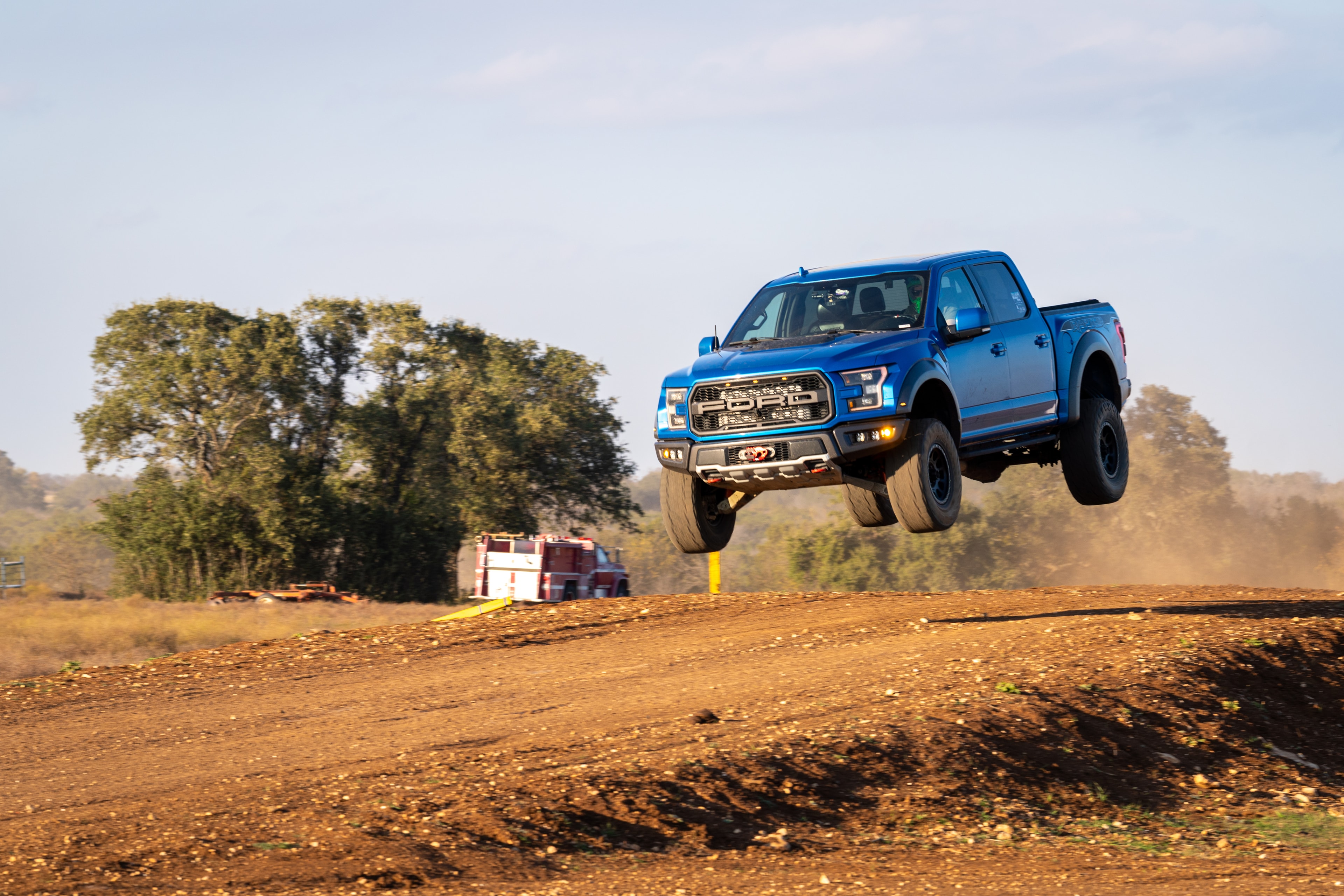 Ford Raptor launching off dirt mound — side angle